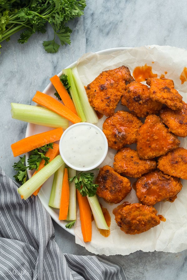 boneless chicken wings overhead on white plate with carrots and celery sticks and grey towel on the side