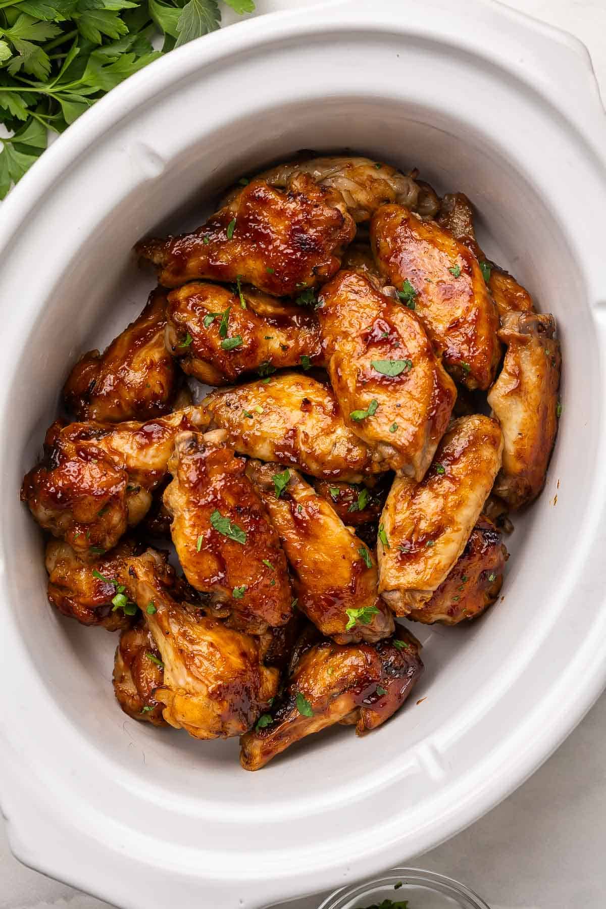 overhead image of chicken wings in a white slow cooker.