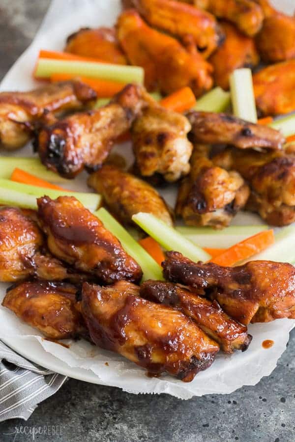 crockpot chicken wings close up on white platter on grey background with carrots and celery sticks in the background