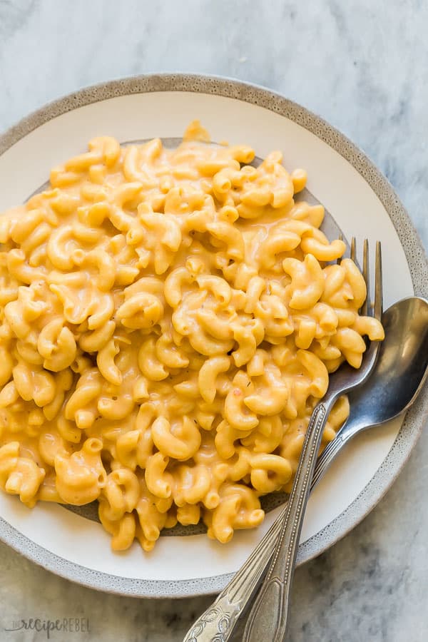 crock pot mac and cheese overhead on grey and white plate with fork and spoon stuck in