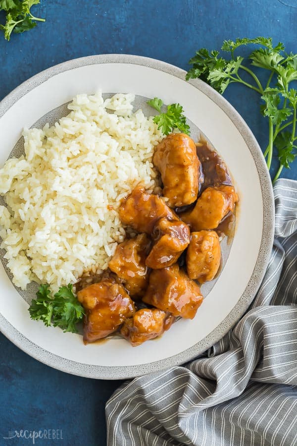 crockpot orange chicken with rice on grey plate overhead on blue background