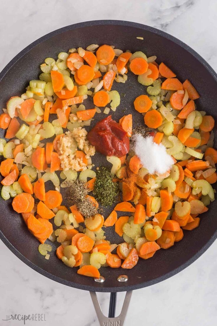 spices and tomato paste added to vegetables in black skillet