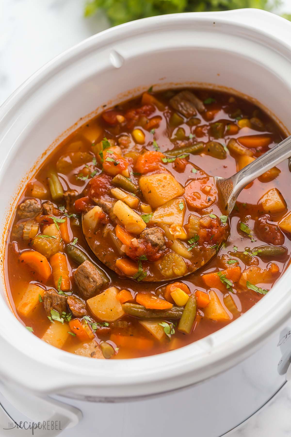 close up image of metal ladle scooping beef vegetable soup from slow cooker