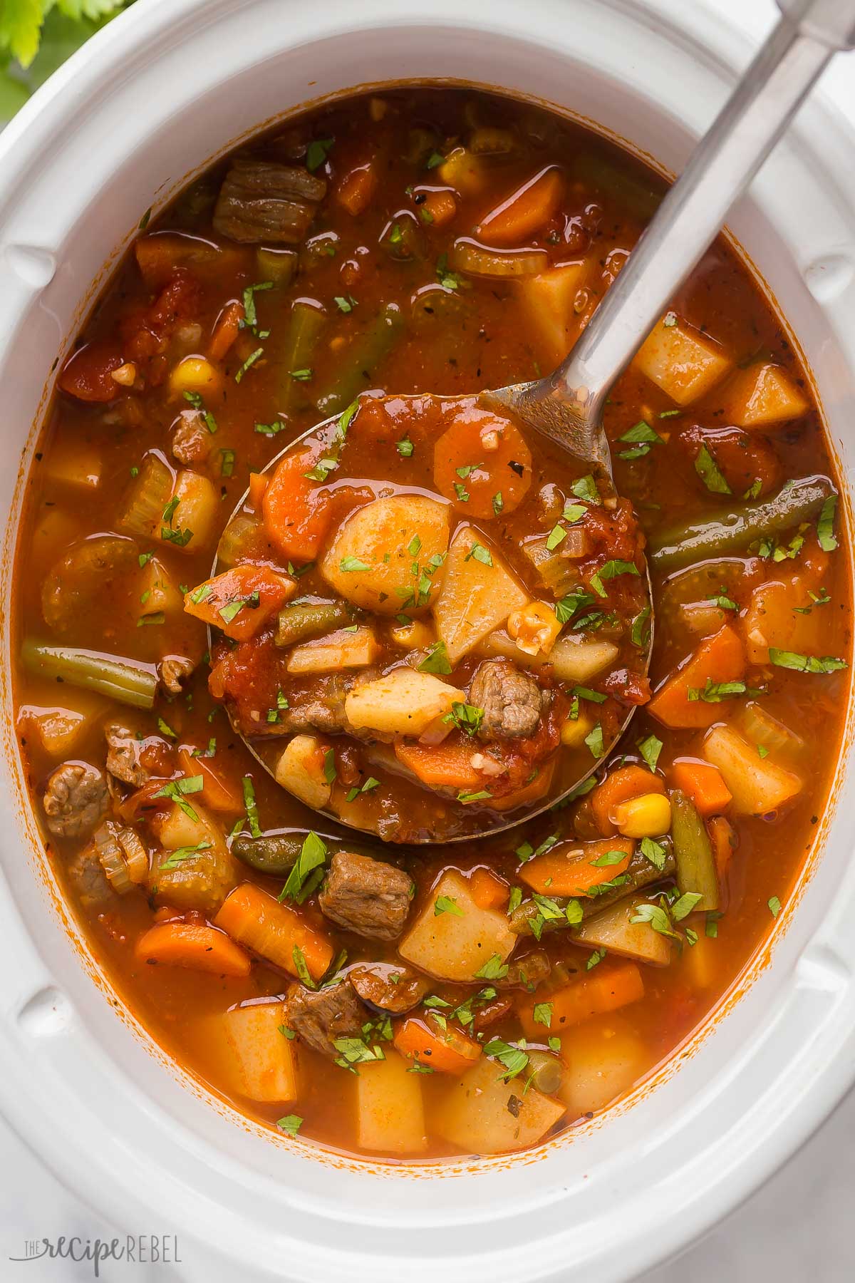 overhead image of beef vegetable soup in crockpot with metal ladle