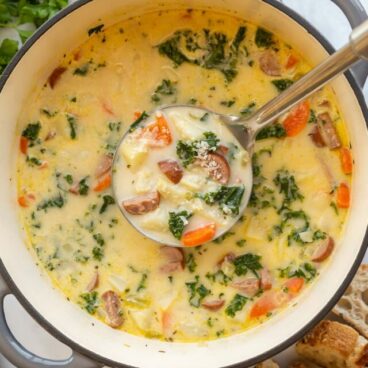 metal ladle scooping sausage potato soup out of dutch oven.