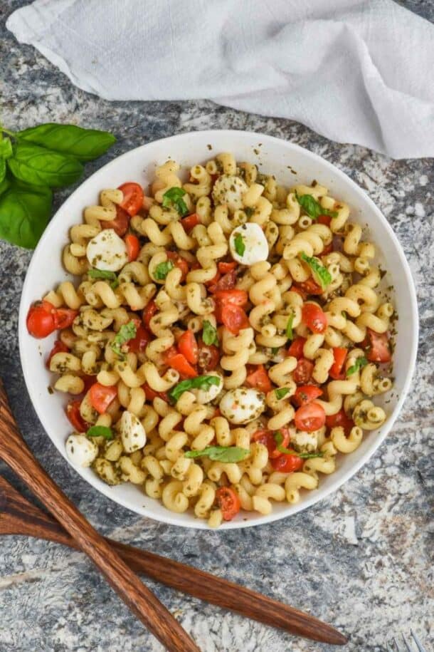 pesto pasta salad overhead in white bowl with wooden spoons on the side