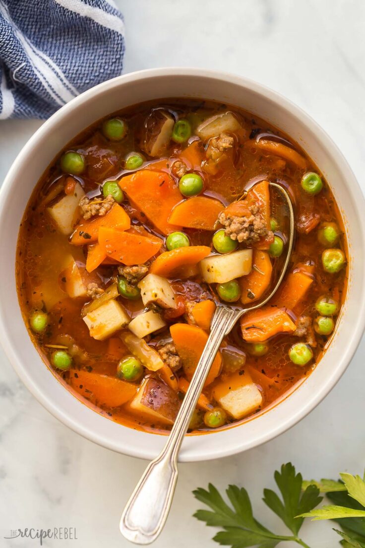 This Hamburger Soup recipe is hearty and comforting for chilly days! It's loaded with vegetables, ground beef, potatoes and can be cooked on the stove top or the crock pot! Includes how to recipe video #soup #recipe #dinner | easy soup recipe | healthy soup recipe | easy dinner ideas | easy recipe | ground beef recipe | healthy dinner overhead image of bowl of hamburger soup with spoon stuck in