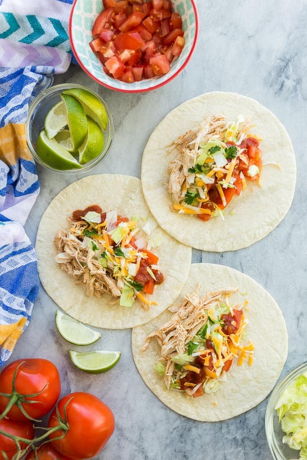 instant pot chicken tacos on flour tortillas overhead on marble with lime wedges and fresh tomatoes on the side