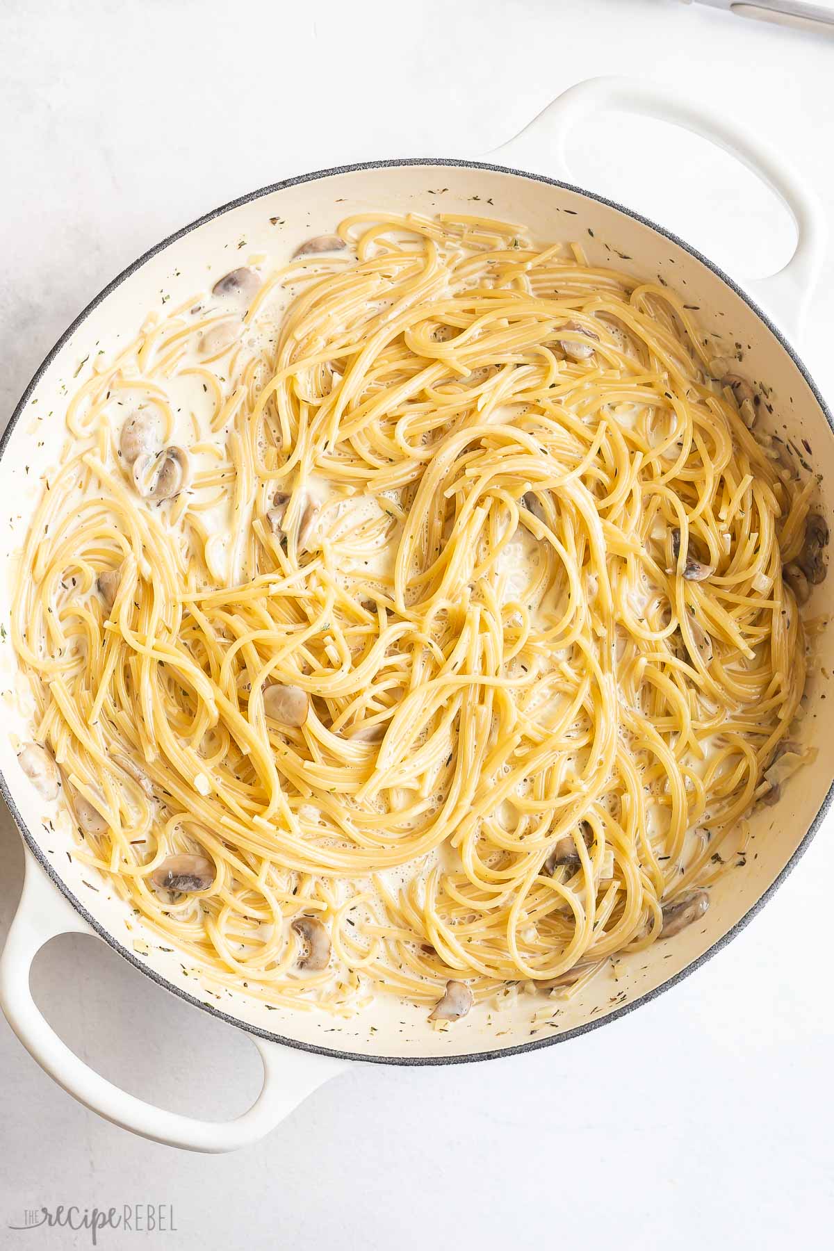 pasta noodles cooked in pan with cream and mushrooms.