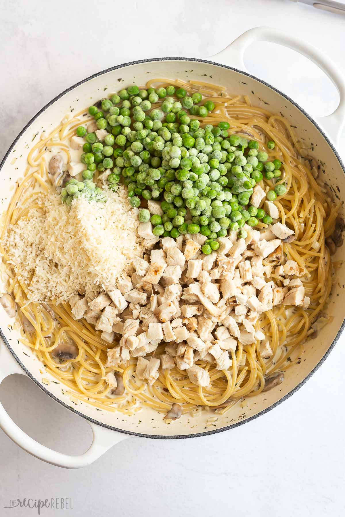 peas parmesan and cooked turkey added to tetrazzini in white pan.