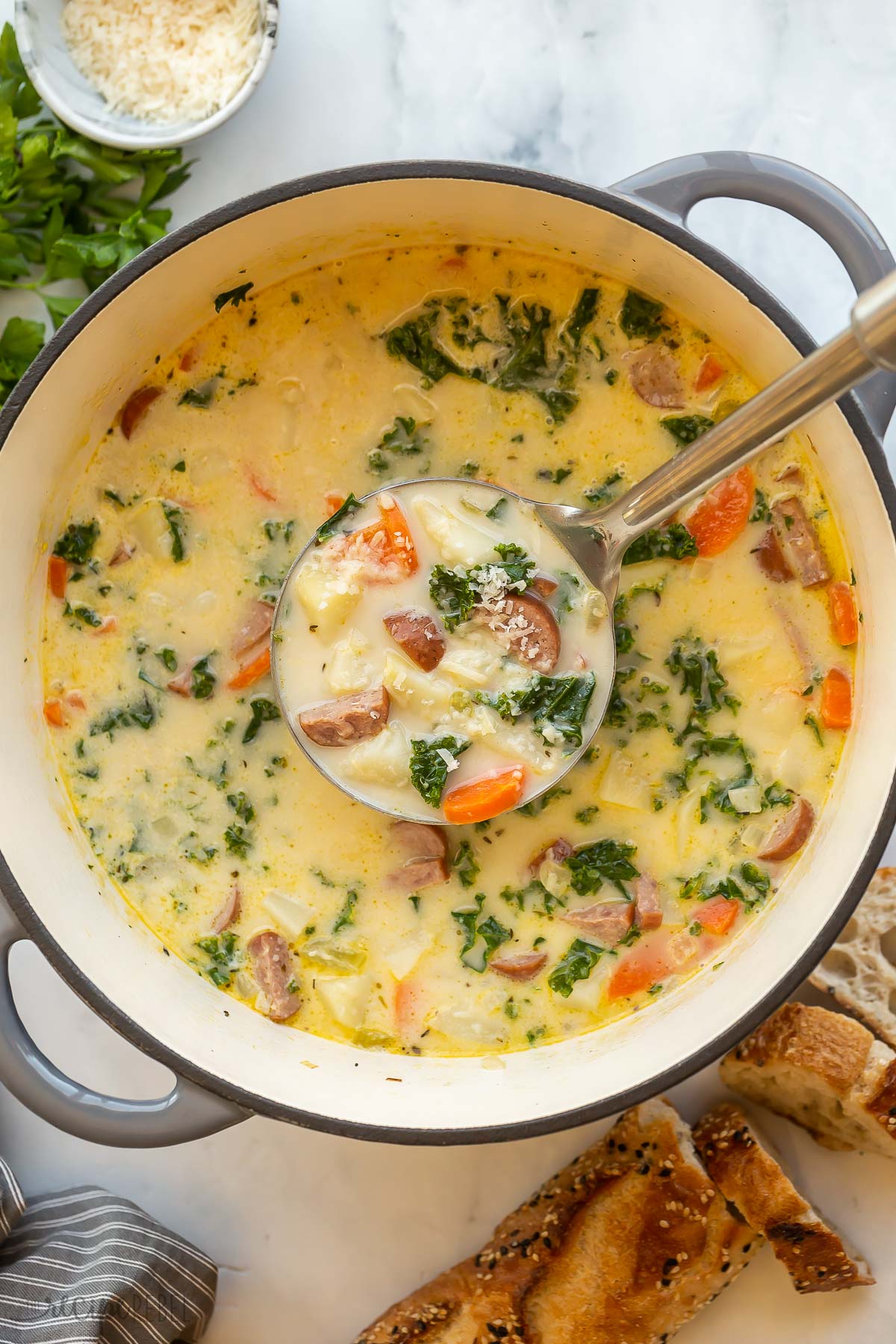 metal ladle scooping sausage potato soup out of dutch oven.