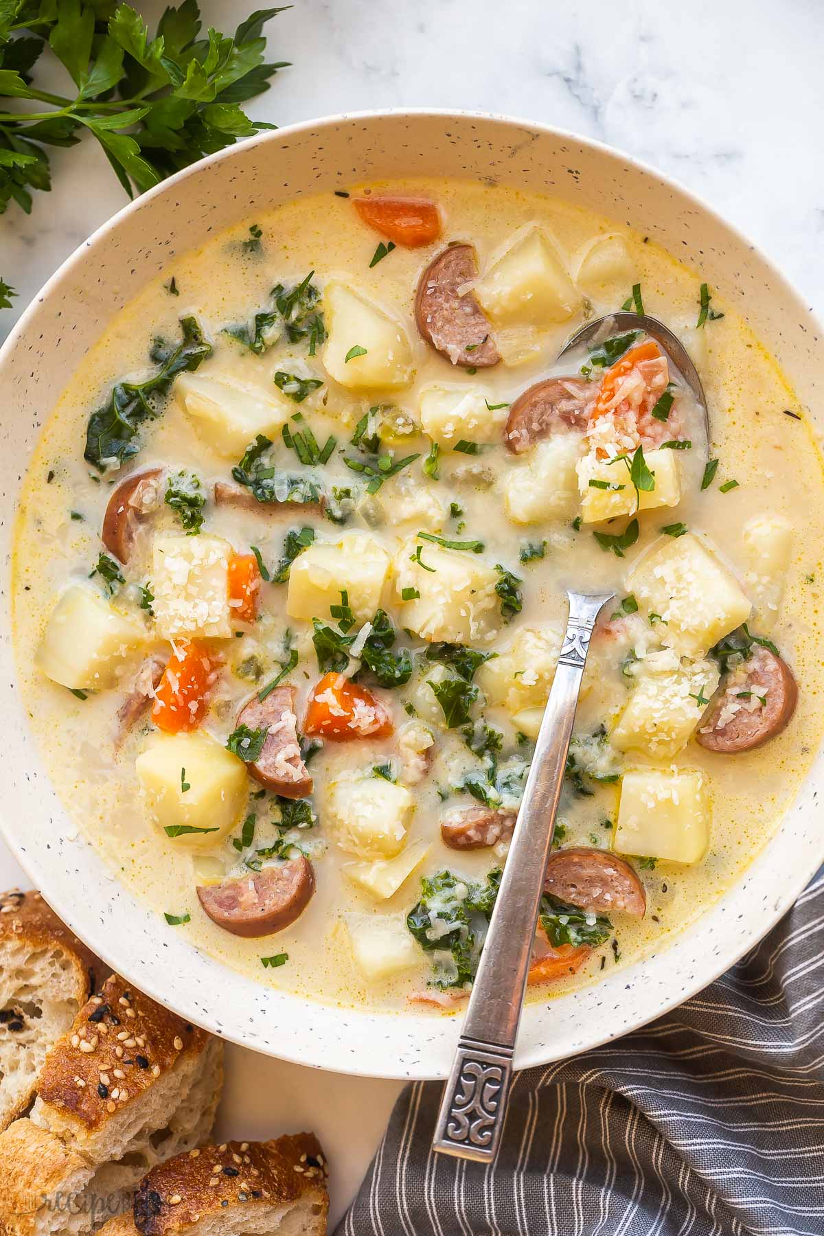 overhead image of sausage potato soup with kale in bowl with spoon.