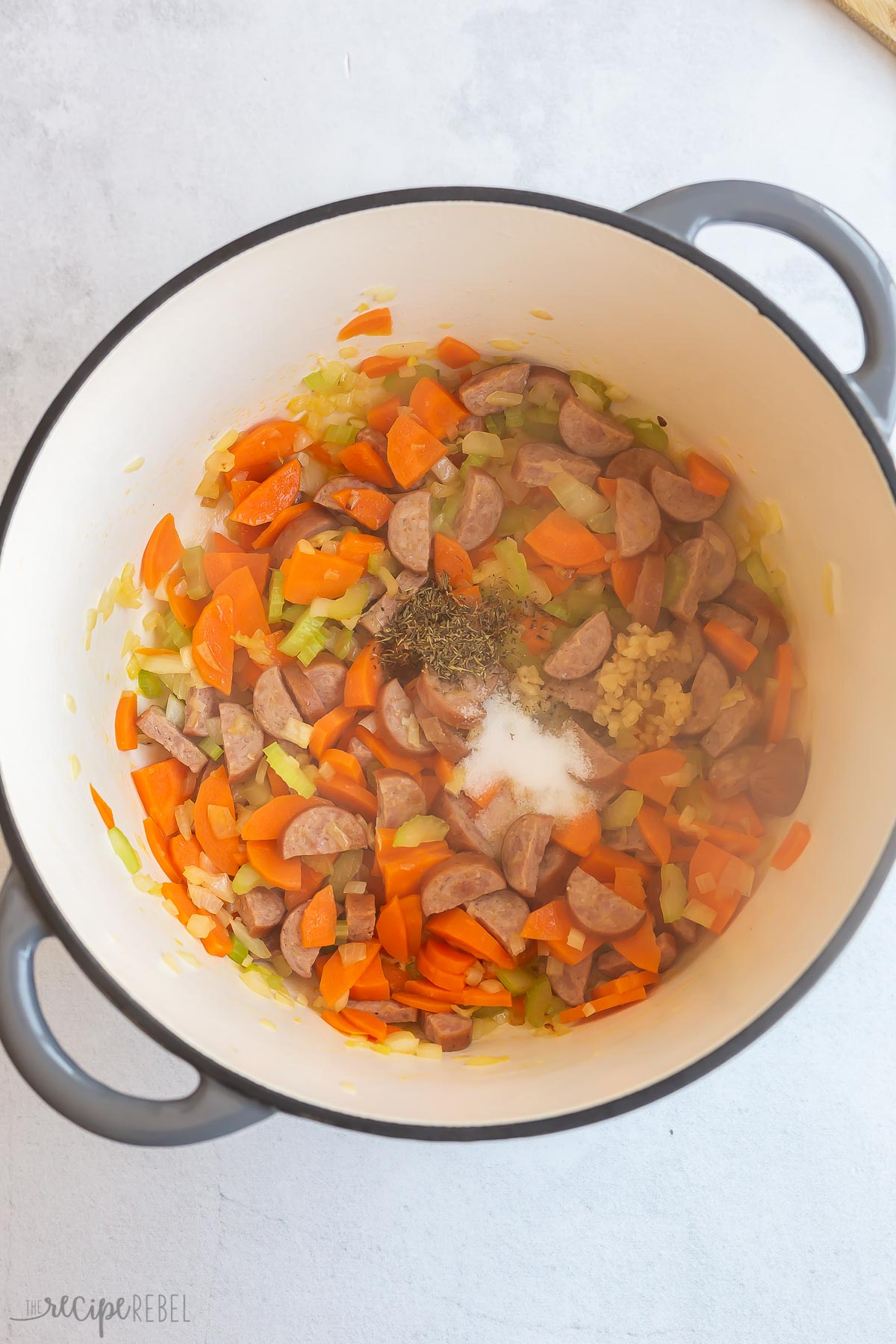 spices added to vegetables and sausage in pot.