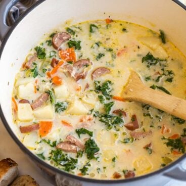 wooden spoon stirring potato sausage soup in large pot.