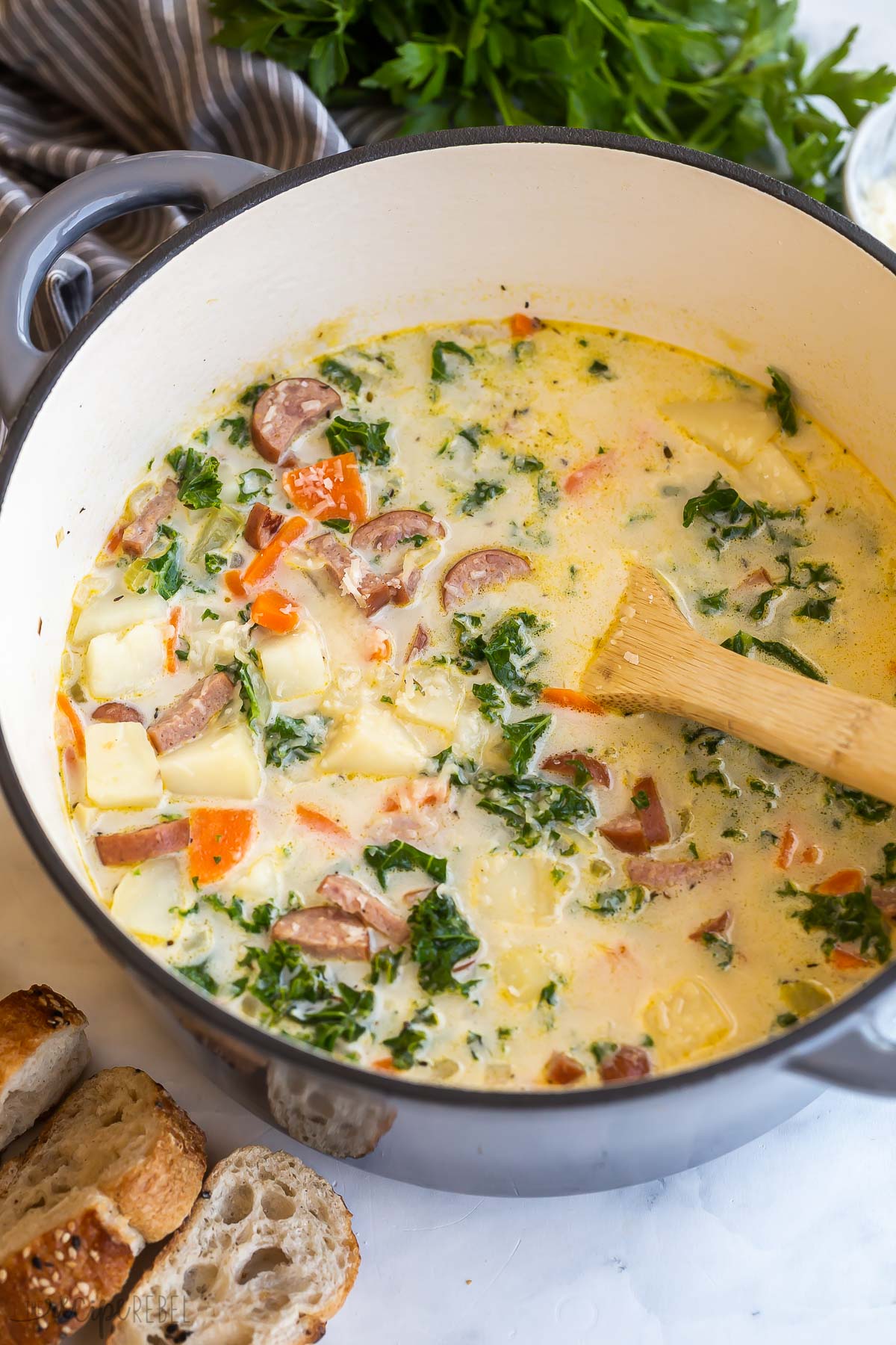 wooden spoon stirring potato sausage soup in large pot.