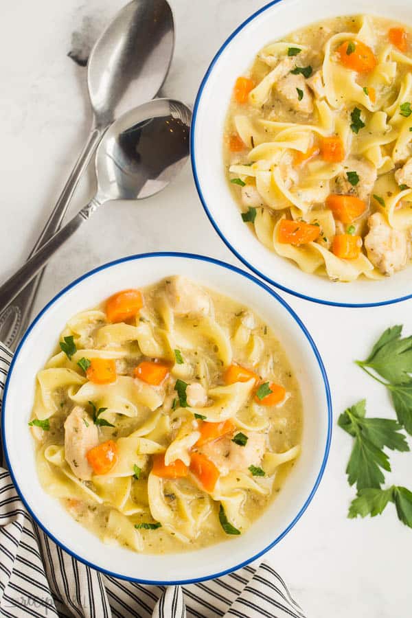 creamy chicken noodle soup in white bowls with blue rim and black and white striped towel on the side