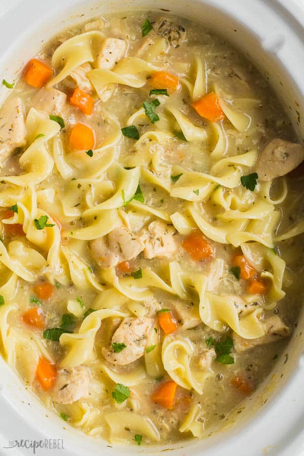 creamy chicken noodle soup in slow cooker overhead close up with fresh chopped parsley