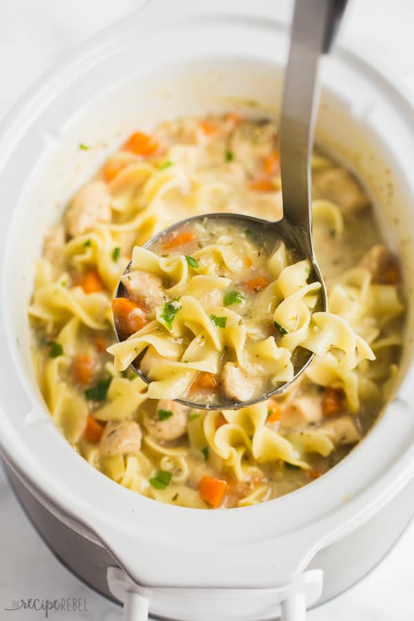 slow cooker creamy chicken noodle soup in a metal ladle above a white crockpot