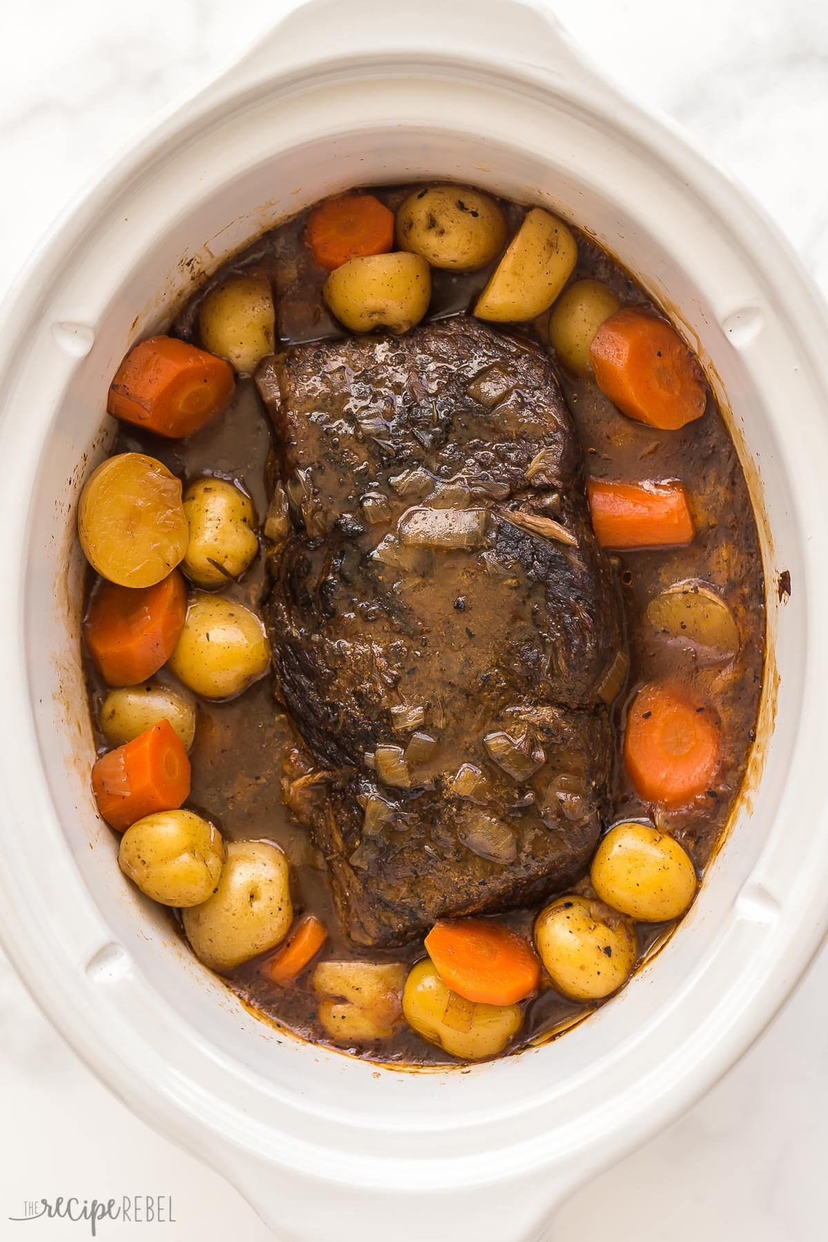 cooked slow cooker pot roast in white crockpot with potatoes and carrots