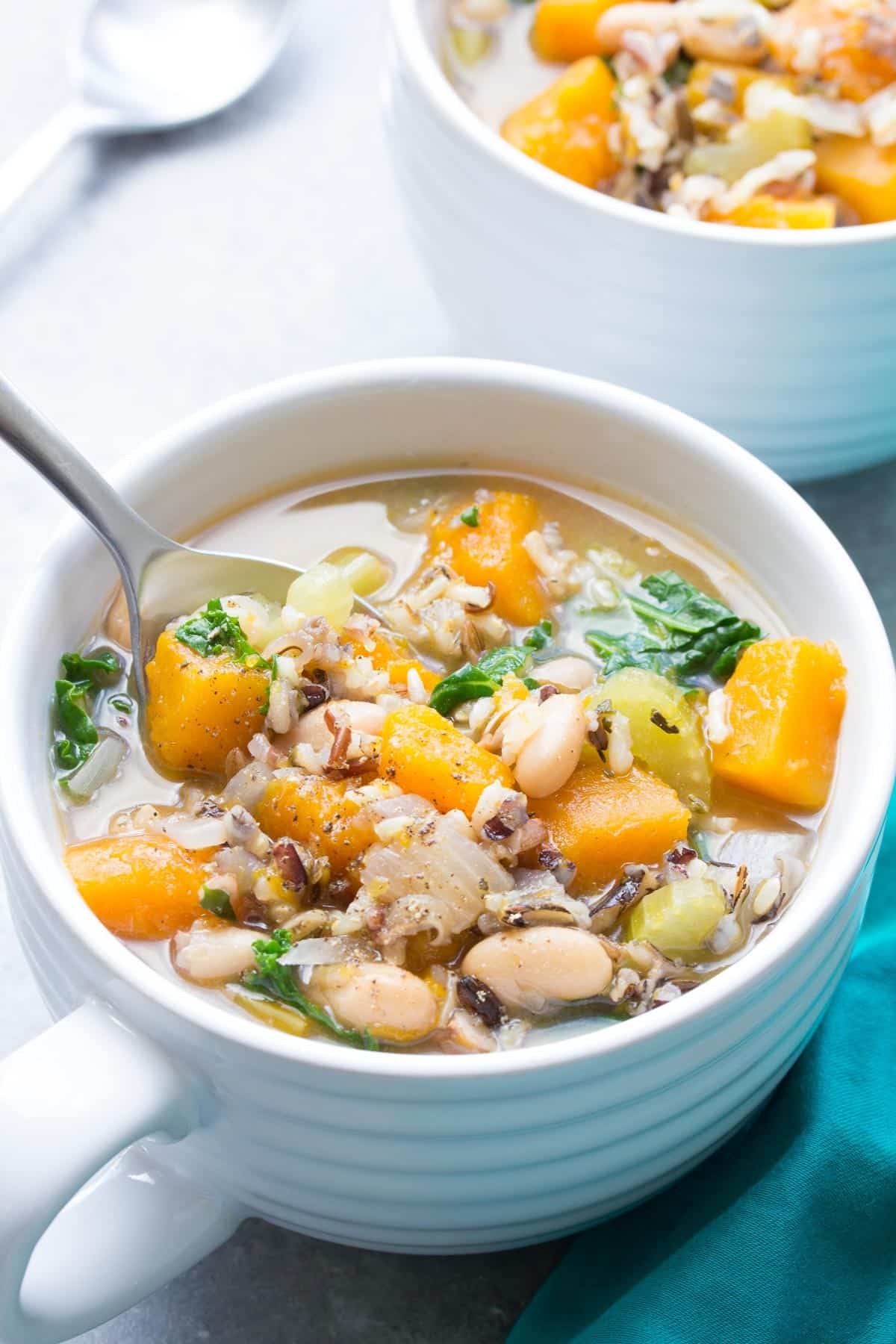 wild rice vegetable crockpot soup in white soup mug with a spoon stuck in the soup