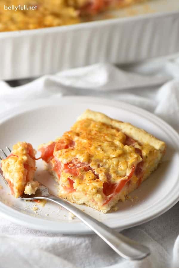 tomato biscuit casserole on white plate with fork taking a bite off the corner