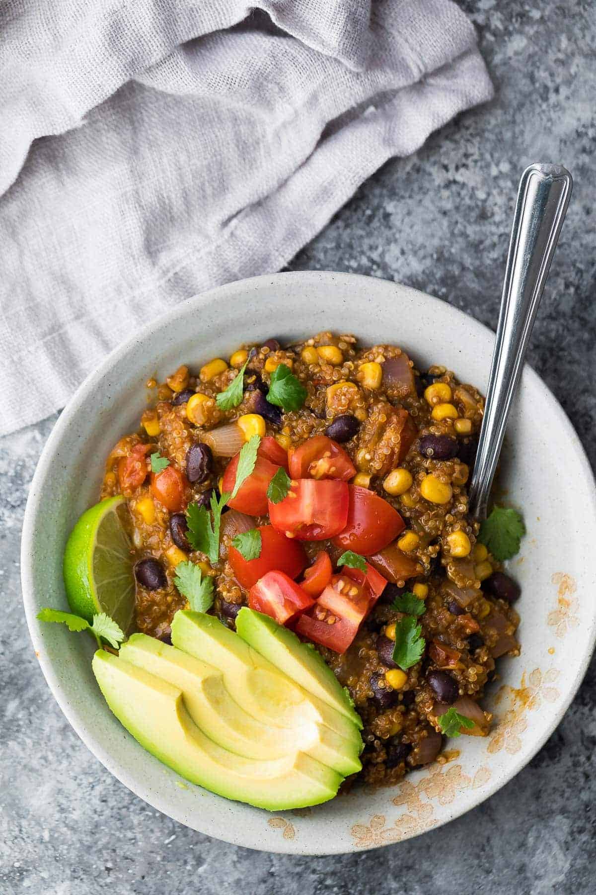 quinoa enchilada casserole overhead on white plate on grey background with avocado slices and fresh tomatoes