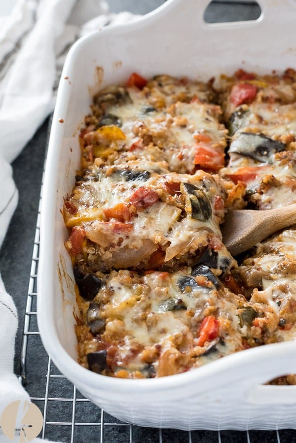 ratatouille casserole cut in pieces in white baking dish with wooden spoon scooping a piece