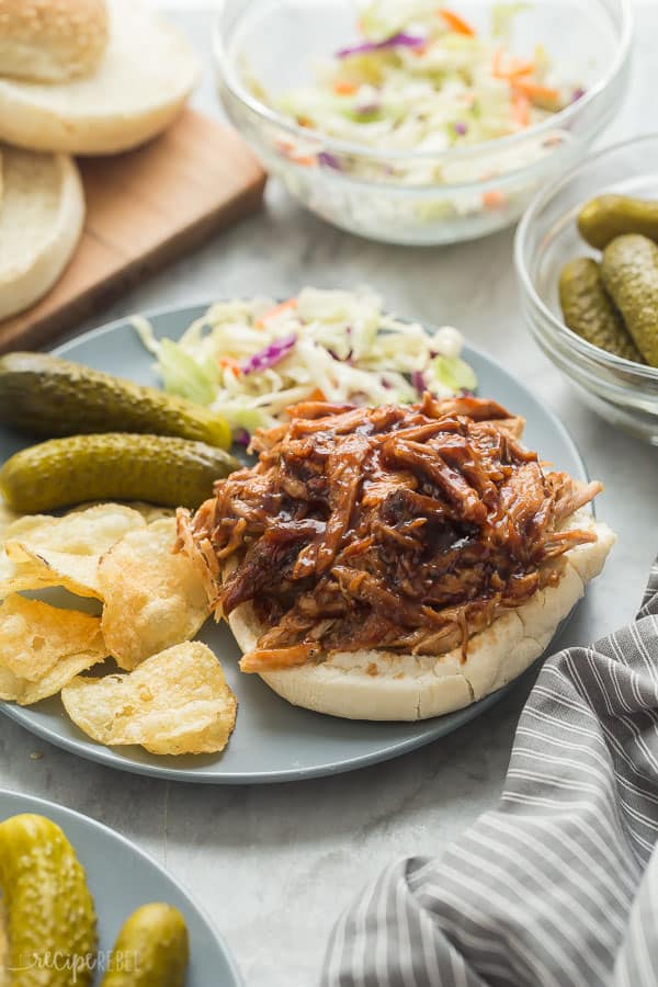 crock pot pulled pork sandwich on grey plate with pickles chips and coleslaw