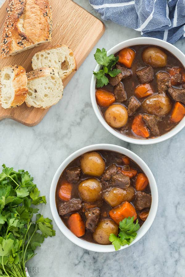 pressure cooker beef stew in white bowls overhead on grey marble background with crusty bread on the side