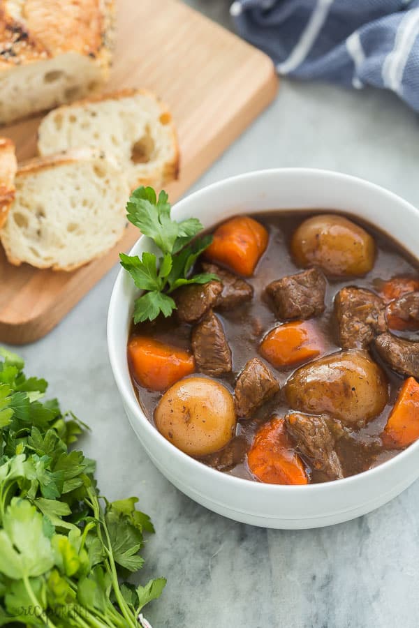 instant pot beef stew in white bowl with parsley and crusty bread in the background