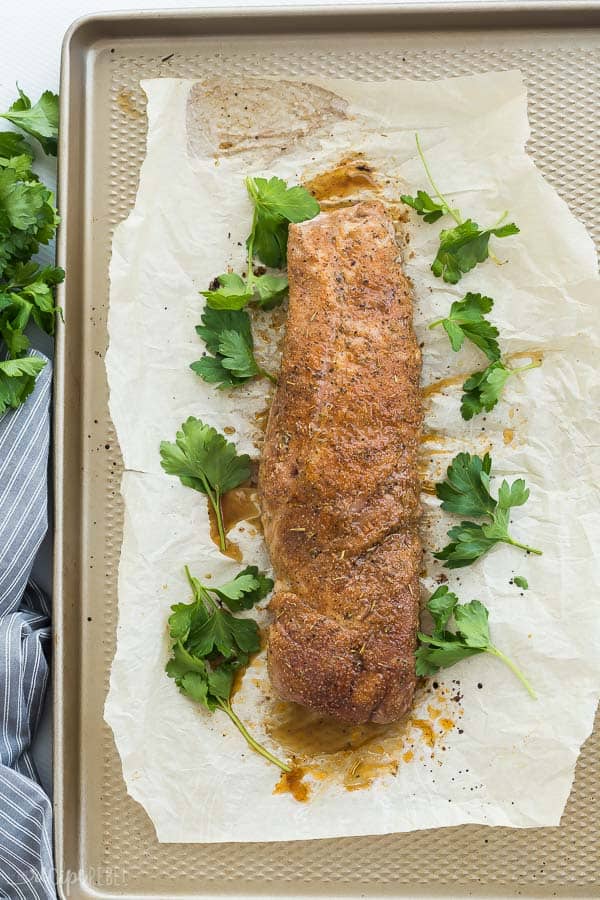 roasted pork tenderloin whole on parchment lined baking sheet with fresh parsley garnish