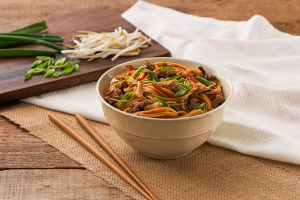 spaghettini stir fry in bowl on wooden background with white towel