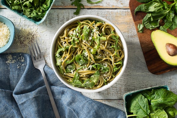 creamy greens pasta overhead in bowl with blue towel on the side