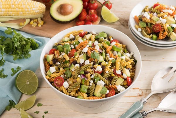 taco pasta salad in bowl with fresh corn avocado and tomato in the background