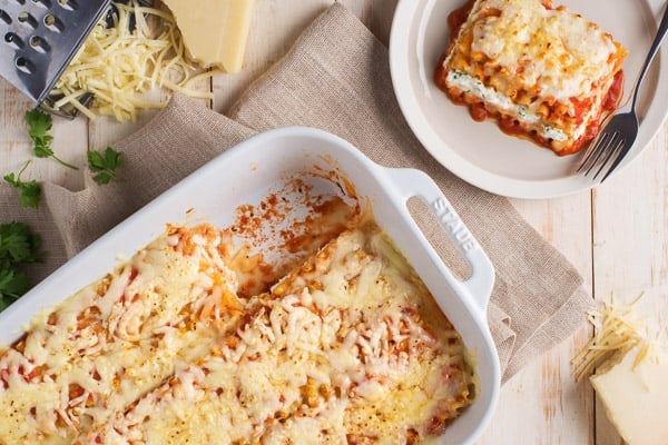triple cheese lasagne in white dish overhead with shredded cheese on the side