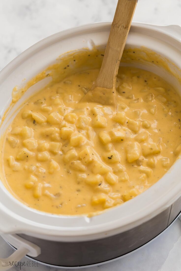 cheesy potatoes in crockpot with wooden spoon