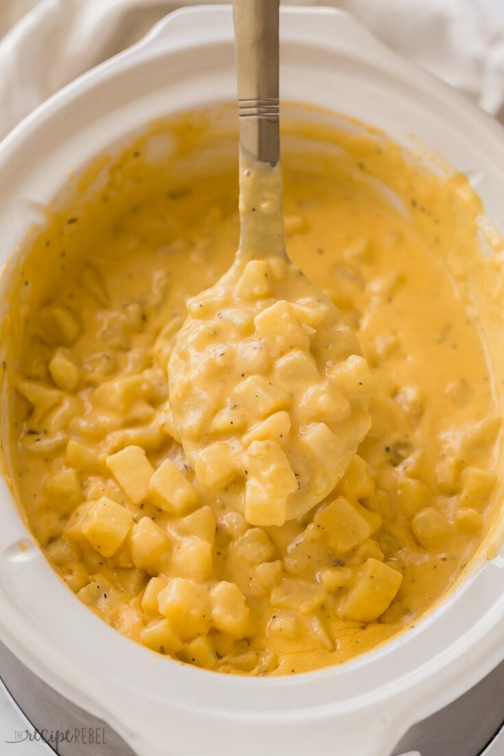 These Crockpot Cheesy Potatoes are an easy side dish, made completely from scratch with fresh potatoes! Perfect for a holiday dinner or potluck! With step by step video. #crockpot #slowcooker | crockpot meals | slow cooker recipes | creamy potatoes | easy dinner ideas metal ladle lifting crockpot cheesy potatoes out of slow cooker