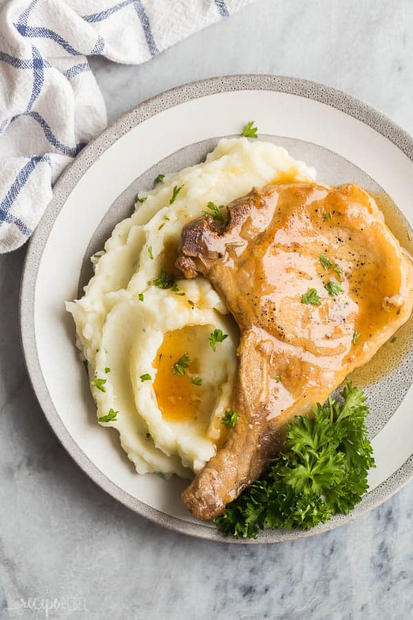 crockpot pork chops bone in overhead with mashed potatoes and fresh parsley on grey plate