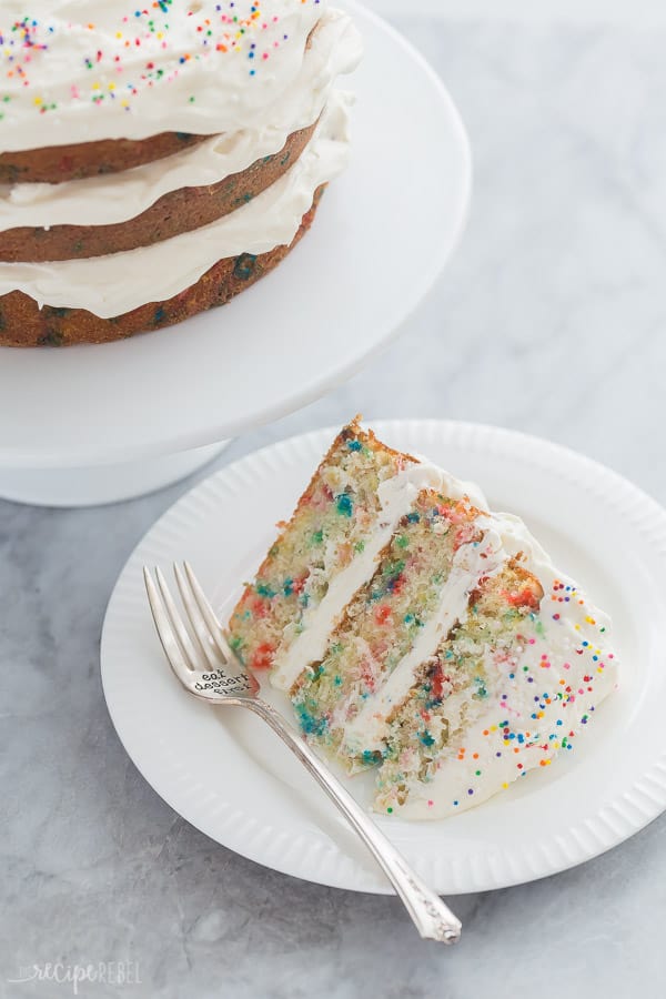 slice of funfetti cake on white plate with fork on grey marble background