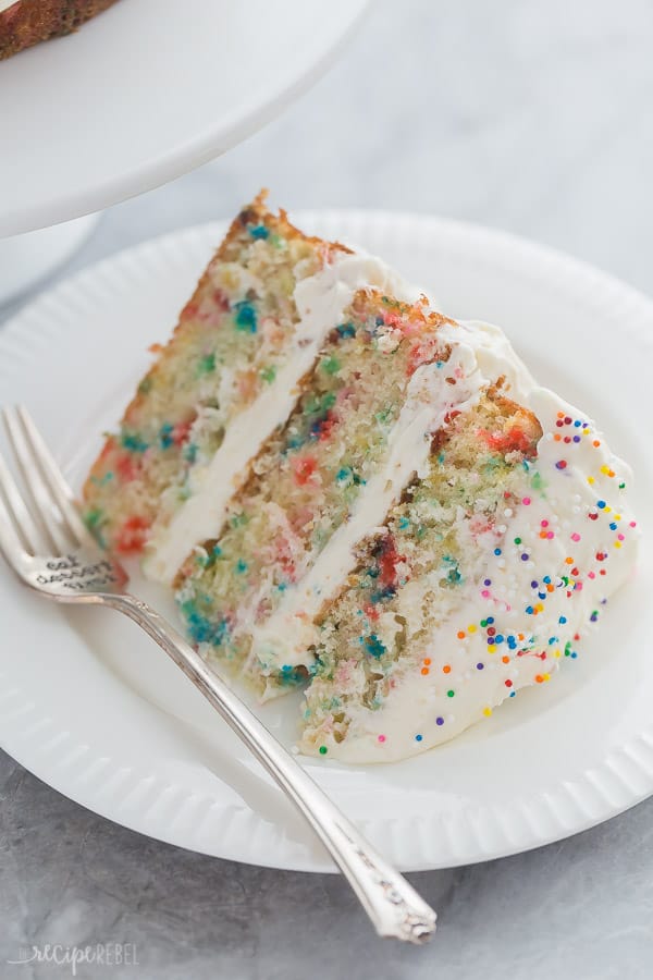 slice of funfetti cake close up on plate 3 layers with whipped cream cheese frosting