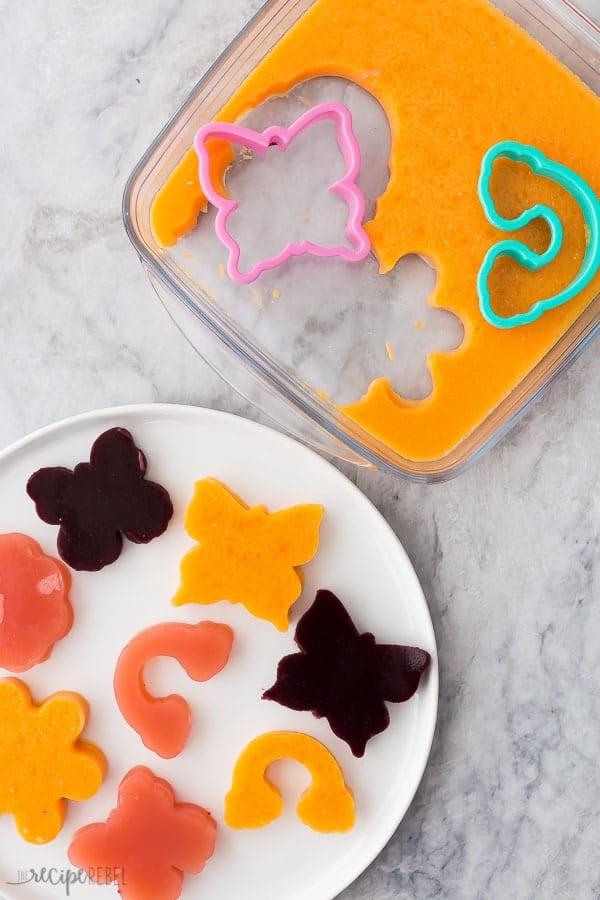 jello jigglers with cookie cutters in glass pan and a white plate with varying flavors and shapes