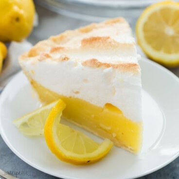 square image of a slice of lemon meringue pie on a white plate.
