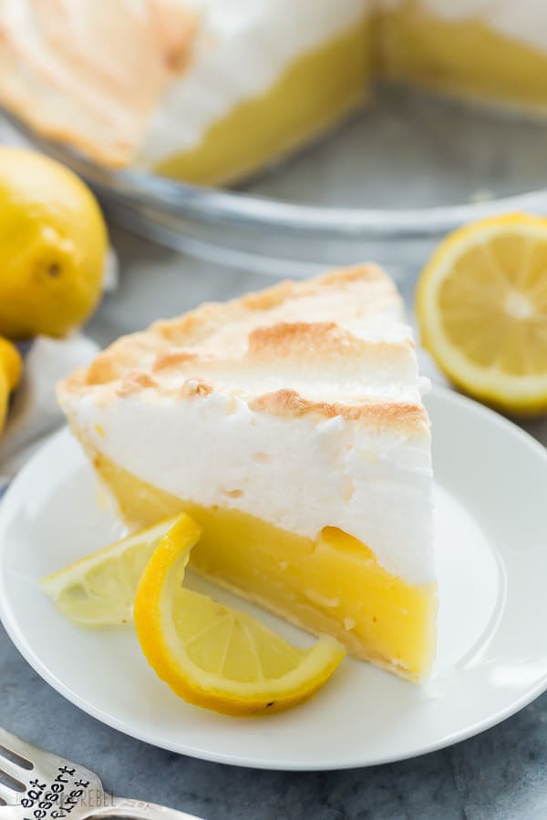 lemon meringue pie slice on white plate with lemon slice on the edge