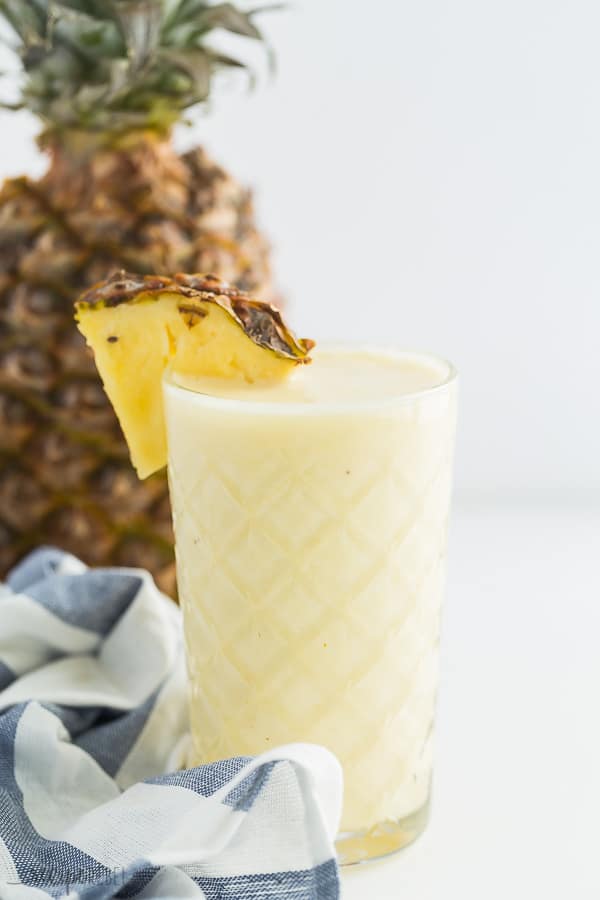 pineapple smoothie in glass with pineapple slice and whole pineapple in background on white background