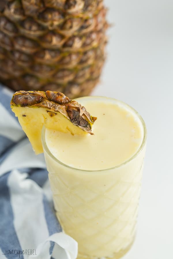 pineapple smoothie in tall glass with blue striped towel and whole pineapple in the background