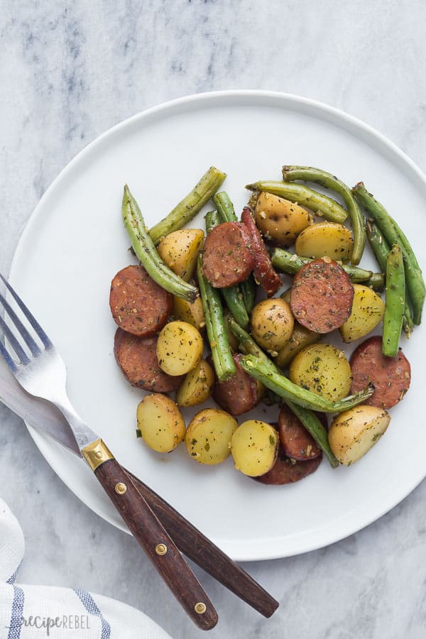 one pan sausage potatoes and green beans on white plate with fork and knife on the side
