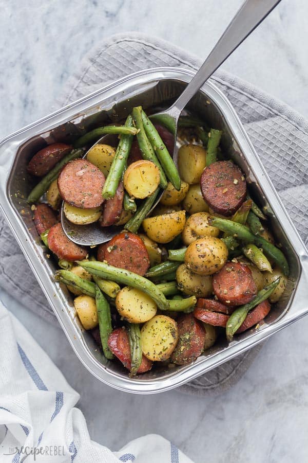sausage potatoes and green beans in one foil pan with metal spoon stuck in the pan