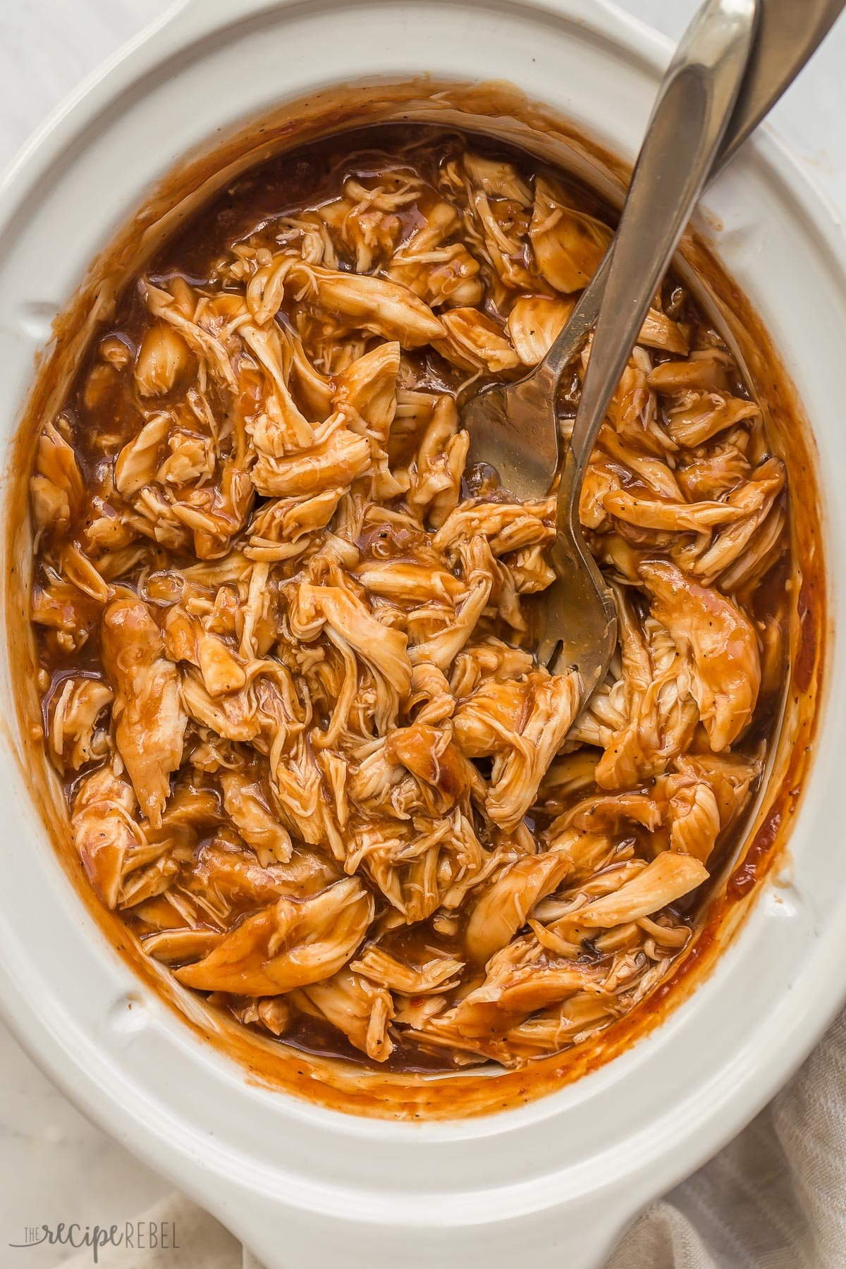 overhead image of barbecue chicken in slow cooker with two forks