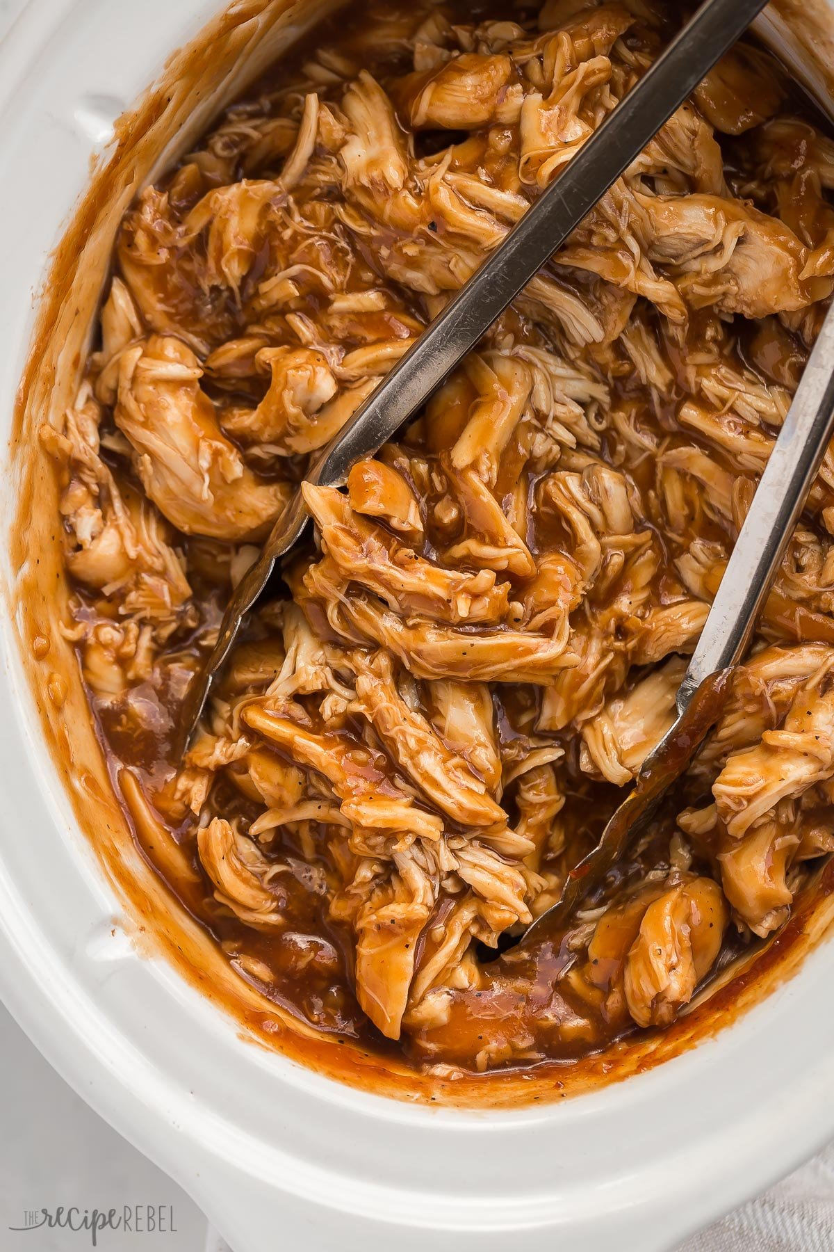 close up overhead image of slow cooker bbq chicken with tongs