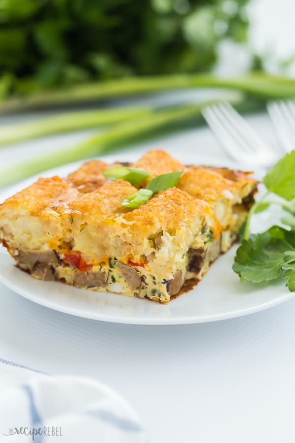 tater tot breakfast casserole piece on white plate with green onions and fresh parsley in the background